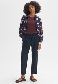 Multicolore blouse met blauwe, witte en bordeaux patronen, gecombineerd met een bordeaux top, marineblauwe broek en bruine sandalen.