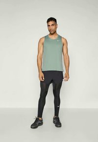 Vêtement de sport pour homme comprenant un débardeur vert clair, un short noir et des leggings noirs avec un logo Nike discret. Design texturé et ajusté.