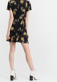 Svart kortärmad klänning med blommiga och paisleymönster, utsvängd kjol, i sällskap med vita klackade ankboots med silverdetaljer.