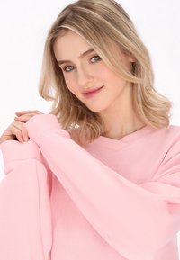 Pullover rosa chiaro con scollatura a V e polsini a costine, caratterizzato da una texture morbida e una vestibilità comoda.