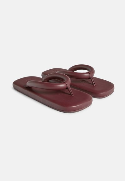 Burgundy flip-flops med en slät, strukturerad sula, som har en rund rem och en rektangulär fotbädddesign.