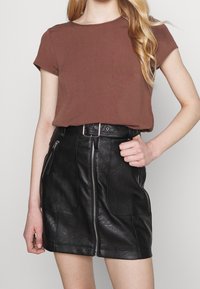 T-shirt marron à manches courtes associé à une mini-jupe en cuir noir avec une fermeture éclair à l'avant et deux poches latérales. Finition en cuir texturé.