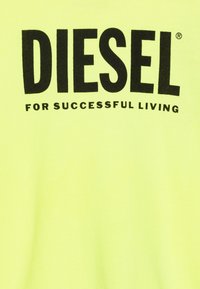 T-shirt gialla neon con testo nero in grassetto che recita "DIESEL PER UNA VITA RIUSCITA." Tessuto morbido, maniche corte, vestibilità casual.
