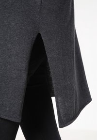 Top in maglia grigia con orlo asimmetrico alto-basso e spacchi laterali; texture morbida e vestibilità comoda. I bordi sono rifiniti con una sottile cucitura overlock.