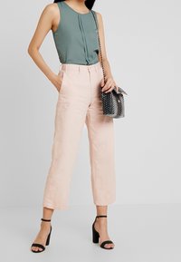 Top verde senza maniche con design a pieghe abbinato a pantaloni a gamba larga rosa chiaro. Accompagnato da una borsa a tracolla con motivo in bianco e nero.