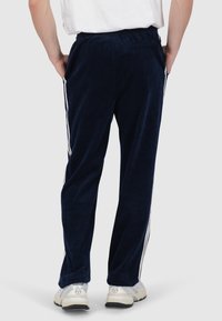 Navy corduroy trainingsbroeken met witte zijstrepen, elastische tailleband en zijzakken. Getailleerde pasvorm, gladde textuur en lichtgewicht.