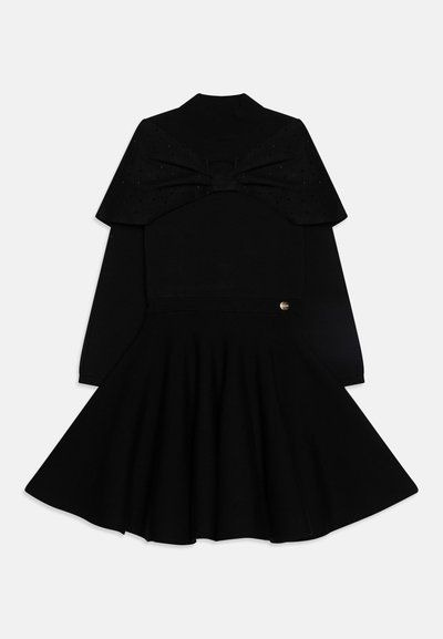 Vestido preto com um corpete ajustado apresentando um detalhe de laço e saia godê. Mangas longas com uma textura suave e um pequeno detalhe dourado de um lado.