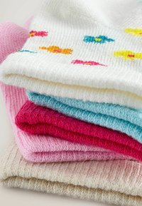 Pinottu pino valkoisia neulottuja villapaitoja, joissa on värikkäitä kukkia: vaaleansininen, magenta, vaaleanpunainen ja beige, vaalealla pinnalla.