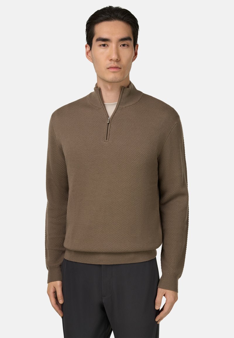 Brązowy sweter z zamkiem na szyi, z fakturowanym splotem, z ściągaczami przy mankietach i u dołu, zestawiony z ciemnymi spodniami. Materiał wydaje się miękki i średniej wagi.