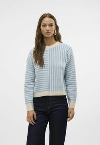 Maglione a righe blu chiaro con vita color crema, caratterizzato da righe di diverse larghezze e collo rotondo. Indossato con jeans scuri.
