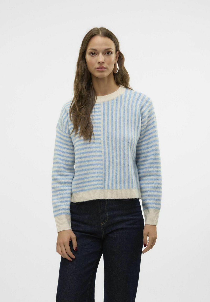 Maglione a righe blu chiaro con vita color crema, caratterizzato da righe di diverse larghezze e collo rotondo. Indossato con jeans scuri.