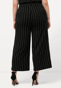 Pantalons large noirs à rayures verticales blanches, avec une taille haute et un tissu doux. Assortis avec des talons noirs à lanières.