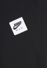 Black fabric jogger with a smooth texture. Features white square patch with "JUMP MAN" in black text and Nike swoosh logo.