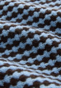 Tissu tricoté avec un motif zigzag alternant bleu clair et marron foncé, montrant la texture et des plis doux.