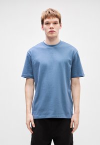 Μπλε βαμβακερή μπλούζα με στρογγυλή λαιμόκοψη, κοντά μανί�κια και μια μικρή λεπτομέρεια κειμένου στο στήθος. Μαλακή υφή και άνετη εφαρμογή.