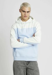 Haut à capuche bleu clair avec des accents blancs. Comprend une poche kangourou, une capuche avec cordon de serrage et des poignets côtelés. Texture lisse et design décontracté.