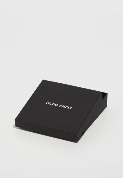 Musta neliölaatikko, joka on valmistettu kestävästä paperista, ja siinä on valkoinen kohotettu teksti "HUGO KREIT" päällä, yksinkertaisella ja minimalistisella muotoilulla.