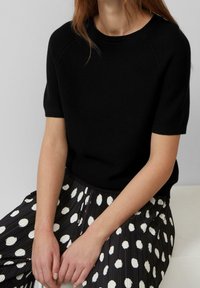 Suéter negro de punto de manga corta combinado con una falda negra con pliegues y puntos blancos. Textura suave con un ajuste relajado.