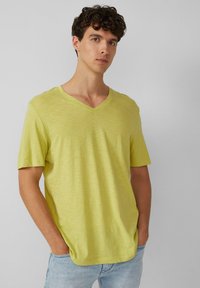 Lichtgele V-hals T-shirt met korte mouwen, gemaakt van zacht materiaal. Glad textuur en een ontspannen pasvorm, gedragen met lichtblauwe jeans.