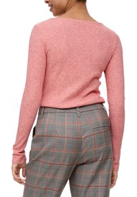 Rippstrick-Pullover in Rosa mit langen Ärmeln und weitem Halsausschnitt, kombiniert mit grauen karierter Hose mit roten Akzenten und Gesäßtaschen.