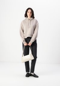 Sudadera corta gris claro con logo, jeans rectos negros y un pequeño bolso crema. Los mocasines negros completan el conjunto.