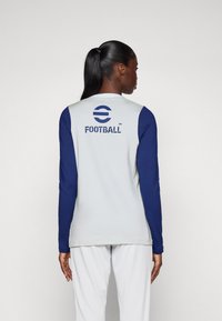 T-shirt de sport à manches longues avec un corps gris clair et des manches bleues. Présente "FOOTBALL" imprimé en bleu foncé à l'arrière. Texture lisse.