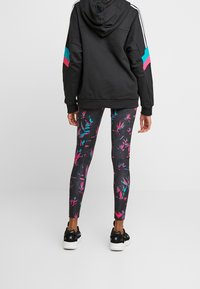 Svart hoodie med färgglada randiga ärmar, i kombination med svarta leggings som har ett livligt rosa och turkosa abstrakt mönster. Svarta sneakers.
