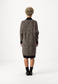 Leopardmönstrad tröjdress i beige och svart, med långa ärmar, ribbade muddar och nederkant, med en avslappnad passform och knälång design.
