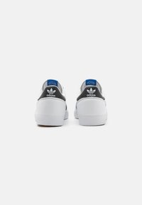 Hvite sneakers med svarte detaljer, glatt syntetisk overdel, polstret krage, blå aksent ved hælen, og teksturerte gummisåler.