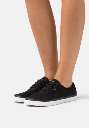 Black canvas sneakers with white rubber soles, round toe, and black laces. Features a small logo accent on the side.