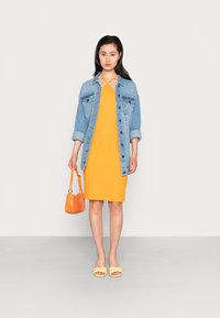 Vestido justo amarelo, jaqueta de ganga, chinelos amarelos e bolsa laranja. Apresenta botões, mangas enroladas e um decote com tiras cruzadas.