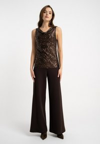 Brązowy top bez rękawów z cekinami i drapowanym dekoltem, zestawiony z luźnymi, ciemnobrązowymi spodniami i szpilkami z ostrym noskiem. Prosty, elegancki design.