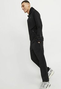 Black athletic tracksuit featuring a zip-up hooded jacket and tapered pants. The fabric is smooth with a slight sheen, designed for comfort.