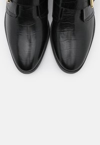 Botas de tobillo de cuero negro con relieve de cocodrilo y punta afilada, con una textura suave y dos hebillas metálicas en la parte superior.