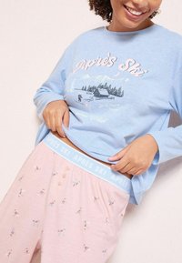 Hele sinine pika varrukaga särk, mille peal on "Après Ski" graafika. Roosa pidžaama püksid suusataja mustriga ja elastse vöökohtadega. Pehme puuvillane kangas.