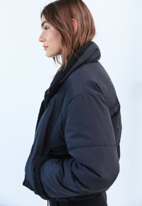 Giacca nera imbottita con colletto strutturato, polsini elasticizzati e design corto, realizzata in materiale morbido e leggero.