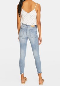 Ljusblå tajta jeans med fransad fåll, kombinerat med en vit ärmlös topp försedd med svarta prickar. Bakvy, minimal hårdvara.