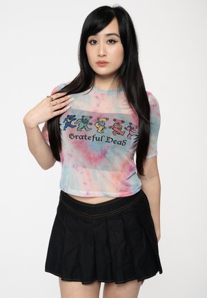 Tie-dye cropped shirt in pastel colors featuring the text "Grateful Dead" and cartoon bears. Paired with a black pleated skirt.