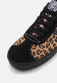 Baskets noires avec une tige en textile à imprimé léopard, des accents en daim noir et des lacets noirs. Semelle texturée pour une meilleure adhérence.