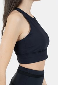 Mustat urheilurintaliivit, joissa on tiukka muotoilu, urheiluolkaimet ja tiukka vyötärö. Valmistettu sileästä, joustavasta materiaalista mukavuutta varten.