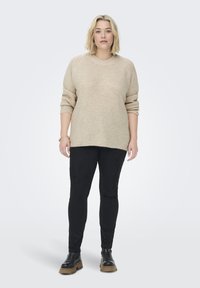 Beiger Strickpullover mit rundem Ausschnitt und Dreiviertelärmeln, kombiniert mit schwarzen Slim-Fit-Hosen und klobigen schwarzen Stiefeln.