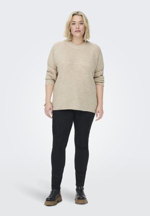 Beiger Strickpullover mit rundem Ausschnitt und Dreiviertelärmeln, kombiniert mit schwarzen Slim-Fit-Hosen und klobigen schwarzen Stiefeln.