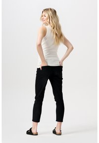 Biała bezrękawnikowa bluzka w połączeniu z czarnymi slim fit dżinsami. Model stoi z boku, prezentując casualowe obuwie i proste włosy.