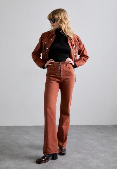 Roestkleurige spijkerjack met studs, zwarte coltrui, bijpassende high-waisted broek en gestreepte blokhak schoenen. Gladde stoftextuur.