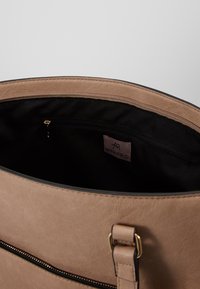 Borsa tote in similpelle color beige con finitura texturizzata, dotata di foderatura nera e tasca interna con zip. Accenti in hardware dorato visibili.