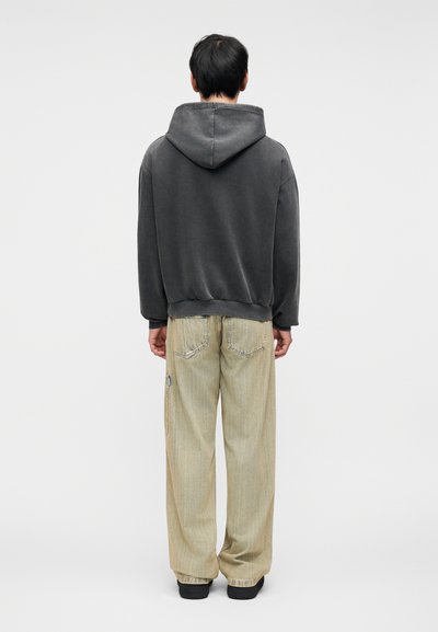 Σκούρο γκρι φούτερ με άνετη εφαρμογή, συνδυασμένο με ανοιχτό μπεζ τζιν παντελόνι φαρδιάς γραμμής με ριγέ υφή και πλαινά τσεπάκια με φερμουάρ.