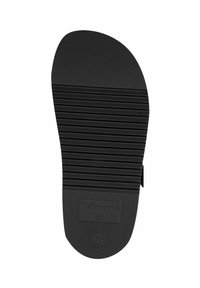 Black rubber shoe sole with textured surface, horizontal grooves, and circular logo. Features raised branding and a smooth edge.