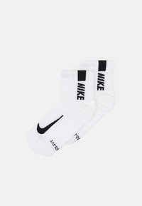 Hvide sokker med et sort Nike-logo og swoosh-design. Medium længde med ribbede manchetter og "Dri-FIT" tekst på siden.