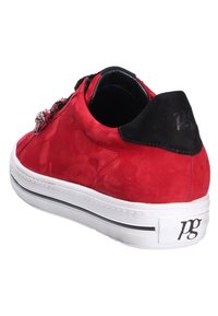 Baskets en daim rouge avec languette de talon noire, semelle blanche avec bande noire et lacets multicolores à motifs, vues de côté arrière.