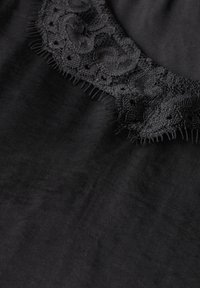 Zwarte stoffen kleding met een kanten rand bij de halslijn, versierd met ingewikkelde patronen en franjes. Glad textiel zonder verdere versieringen.
